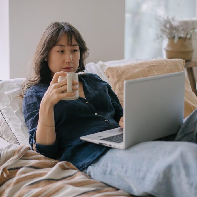 Beautiful young woman working on laptop computer while sitting at the bedroom, drinking a coffee Reach Higher Finish Line Scholarship